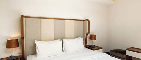 A hotel room with a large bed, wooden headboard, bedside tables with lamps, and an air conditioning unit on the ceiling.