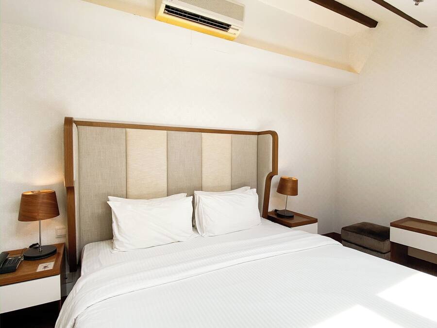 Habitación de hotel con una cama grande, cabecera de madera, mesitas de noche con lámparas y un equipo de aire acondicionado en el techo.