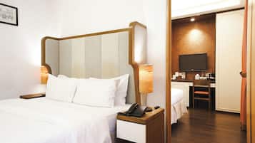 A hotel room with a bed, bedside lamps, a telephone, a desk with a television, and a bathroom visible through an open door.