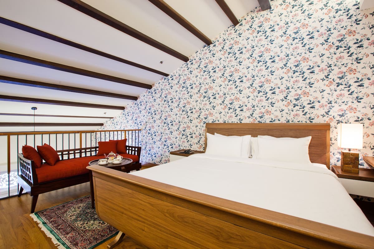A bedroom with a wooden bed, a red sofa, a nightstand, and a floral-patterned wall.
