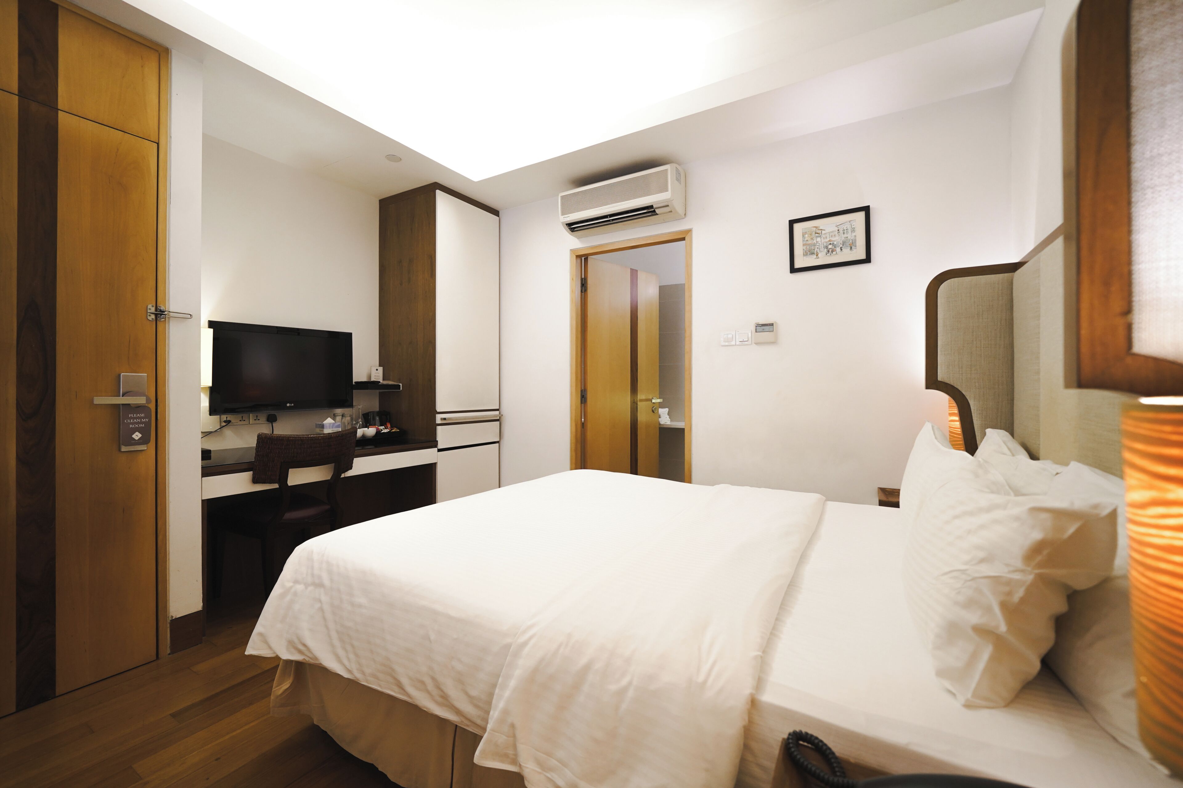 Quarto de hotel com cama, escrivaninha, televisão, aparelho de ar condicionado e porta de acesso a um banheiro.