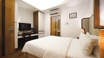 Quarto de hotel com cama, escrivaninha, televisão, aparelho de ar condicionado e porta de acesso a um banheiro.