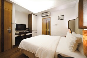 A hotel room with a bed, a desk, a television, an air conditioning unit, and a door leading to a bathroom. - The Sultan (Singapore)