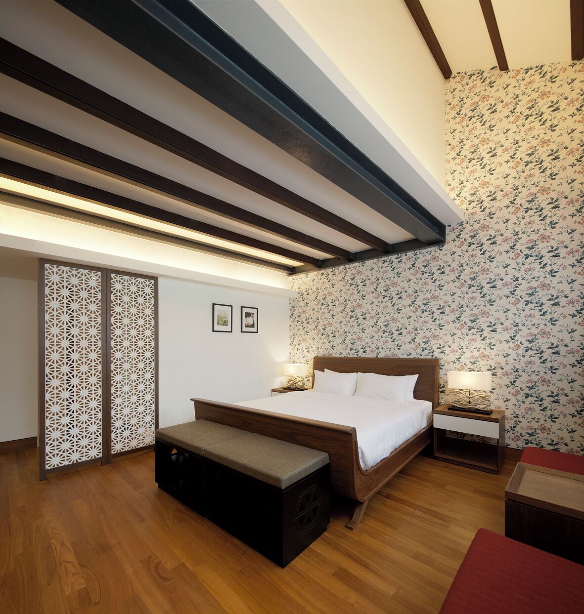 A bedroom with a wooden bed, a bench, a nightstand, and a wall with floral wallpaper.