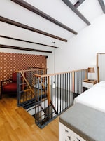 Una habitación con escalera de madera, cama, mesita de noche, lámpara y una silla.