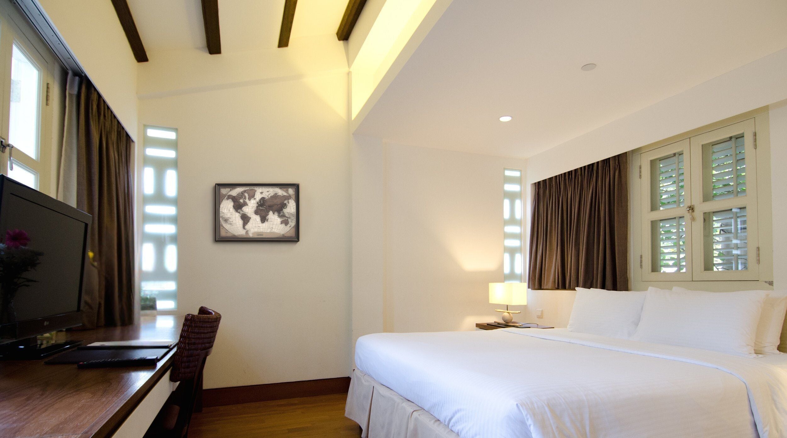 A hotel room with a bed, a desk with a computer, a television, and a world map on the wall.