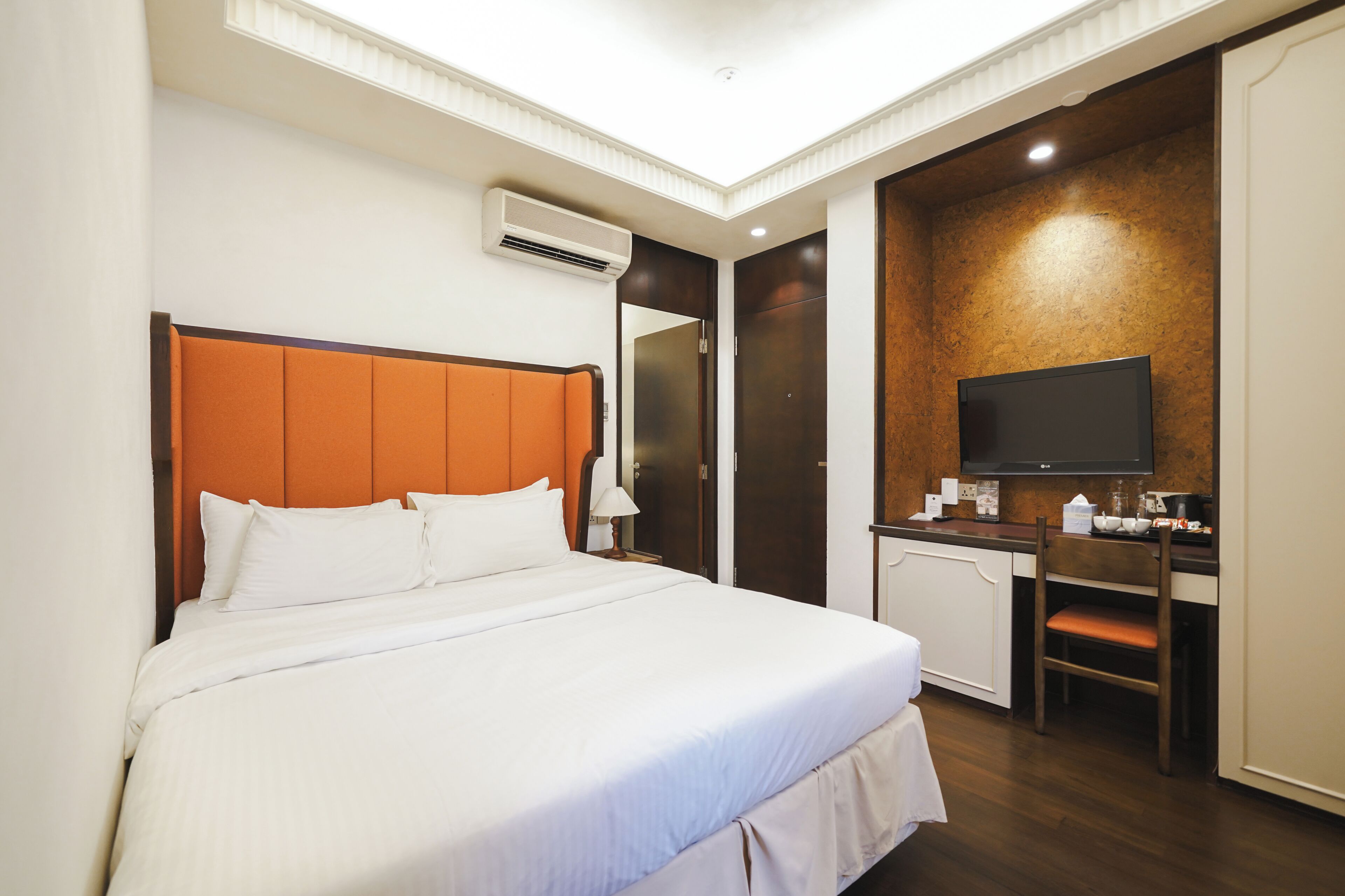 A hotel room with a bed, a desk, a chair, a television, and a mirror.