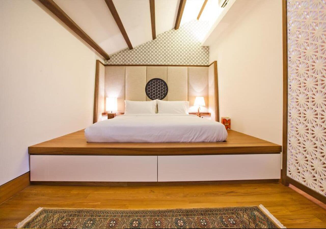 Un dormitorio con una cama baja tipo plataforma, cabecera estampada, lámparas de noche y un panel decorativo en la pared.