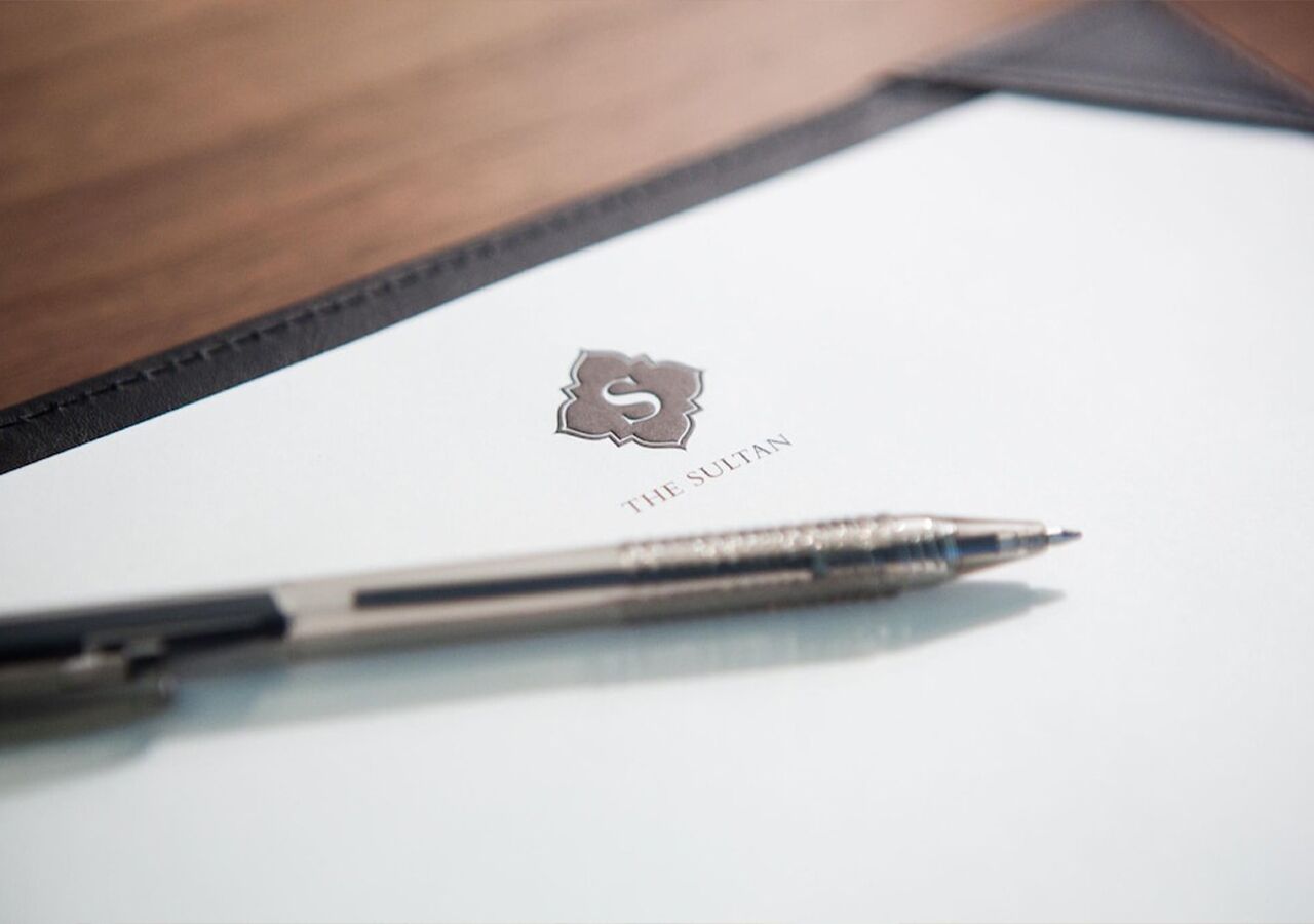 Una pluma sobre una superfície blanca amb un logotip i el text 'THE SULTAN'.