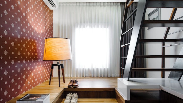 A hotel room with a wooden floor, a desk with a lamp, a pair of shoes, a stack of books, and a staircase.