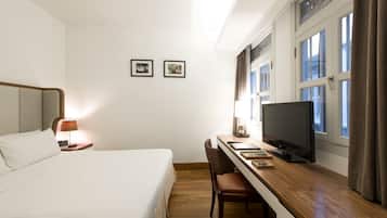 Una habitación de hotel con una cama, un escritorio con televisor, una silla y dos cuadros en la pared.