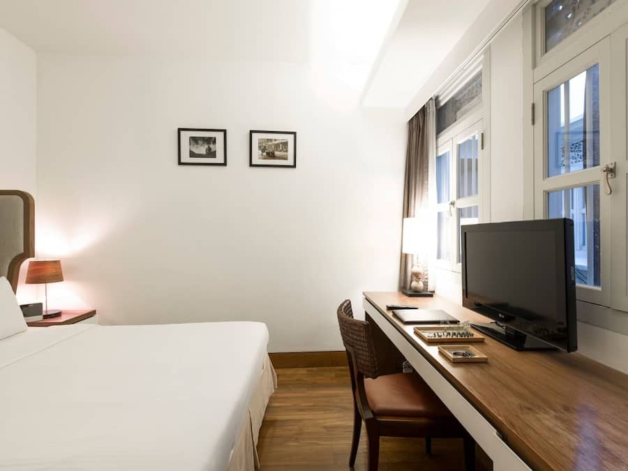 Una habitación de hotel con una cama, un escritorio con televisor, una silla y dos cuadros en la pared.