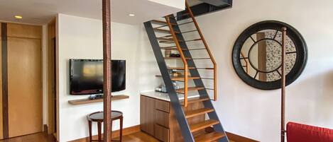 A modern interior with a staircase, a flat-screen TV, a red sofa, and a wooden dining table.