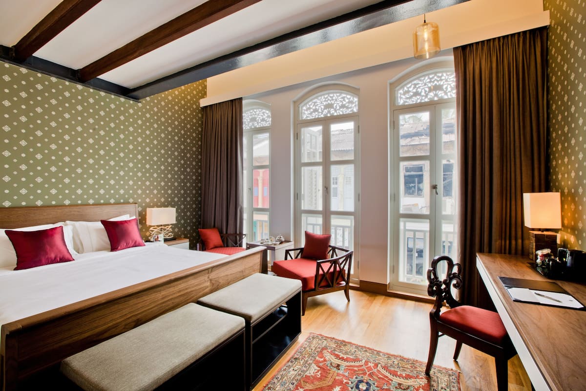 A hotel room with a large bed, a desk, a chair, and a window with decorative curtains.