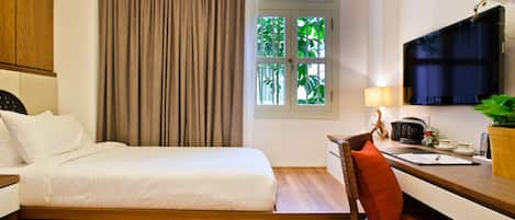 A compact hotel room with a bed, a desk, a chair, a television, and a window with curtains.