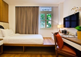 A compact hotel room with a bed, a desk, a chair, a television, and a window with curtains.