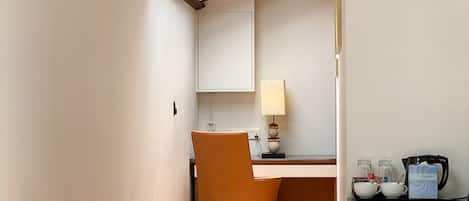Una habitación de hotel con cama, escritorio, silla, lámpara y cafetera.