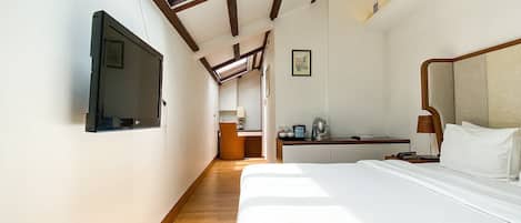 A hotel room with a bed, a desk, a chair, a television, and a skylight.