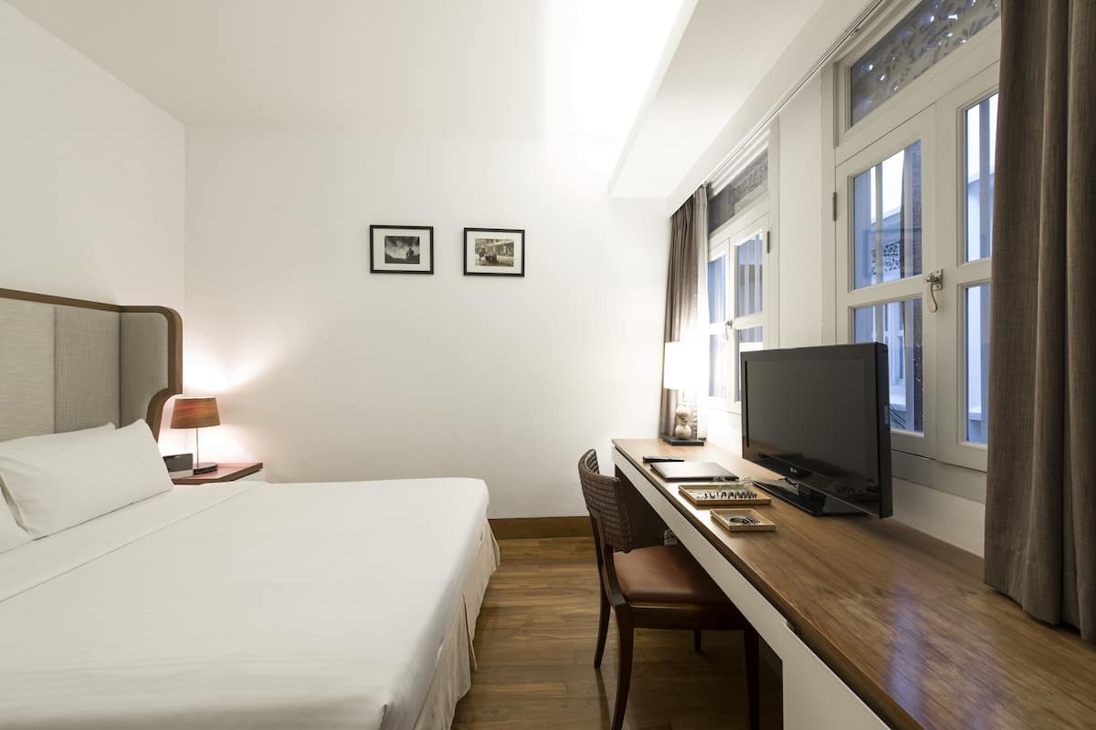 A hotel room with a bed, desk, chair, television, and two framed pictures on the wall.