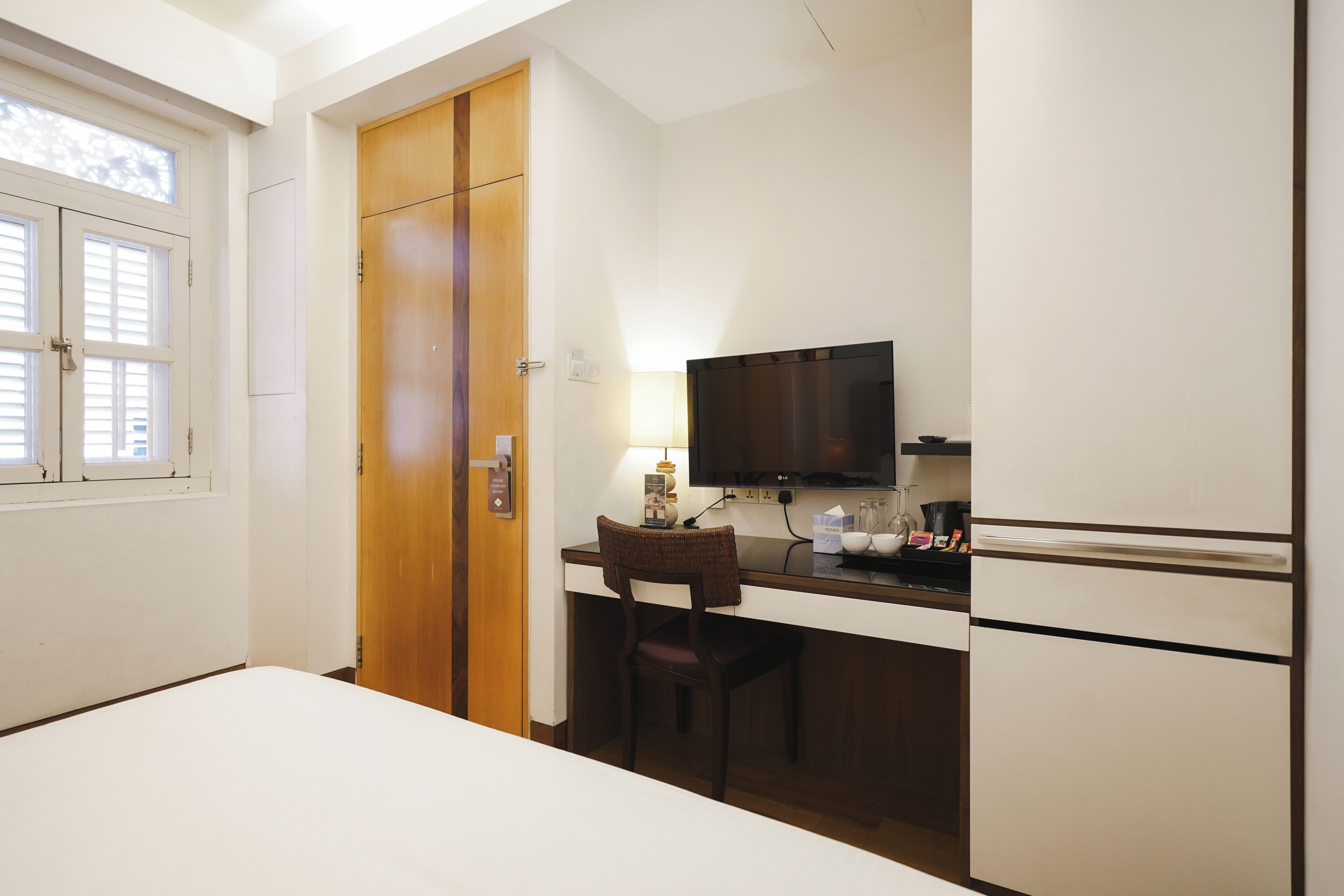 A hotel room with a bed, a desk with a chair, a television, a minibar, and a wardrobe.