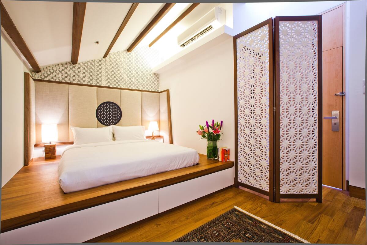 A bedroom with a bed, bedside tables, a decorative wall panel, and a wooden floor.