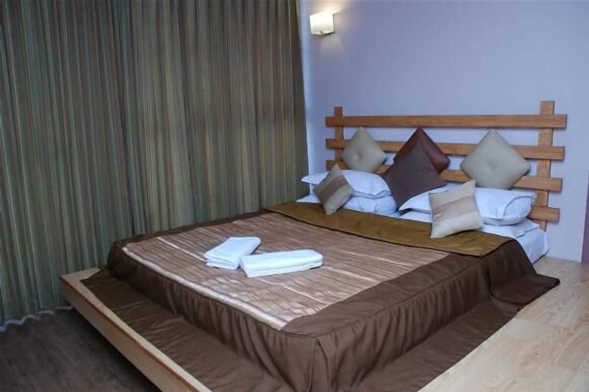 A hotel room with a bed, a wooden headboard, and a curtain.