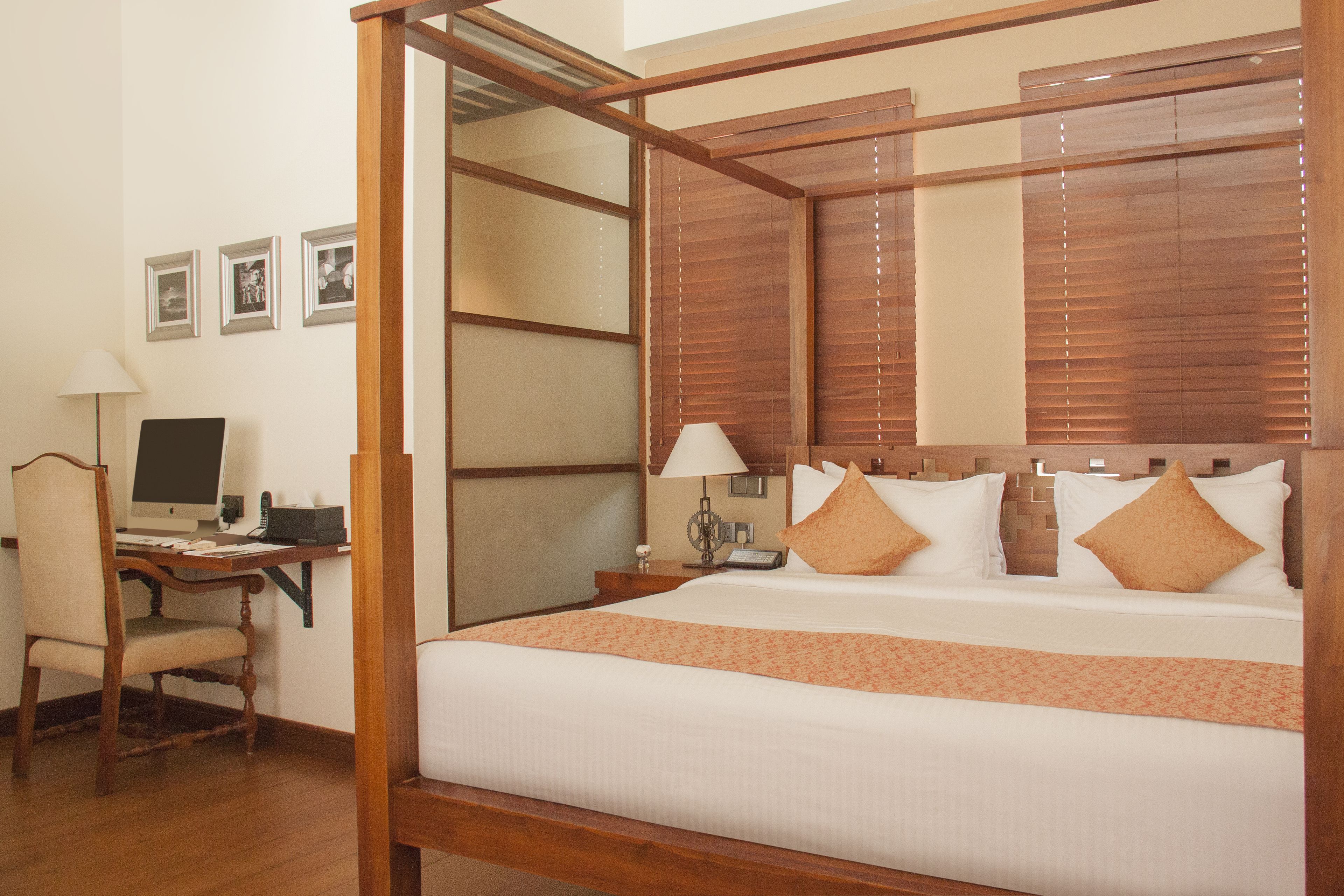 A four-poster bed with a wooden frame, a desk with a computer, and a chair.