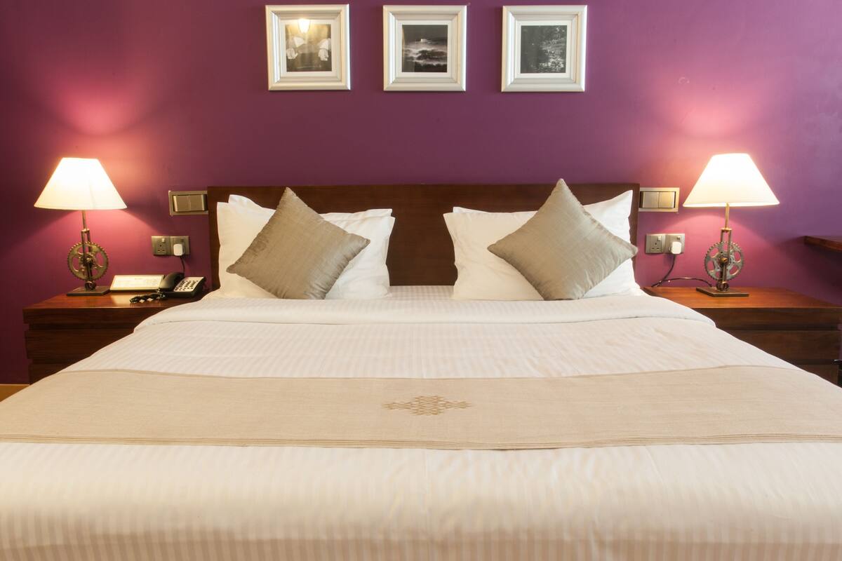 Un letto rifatto con lenzuola bianche e due cuscini decorativi, affiancato da due comodini con lampade e un telefono.