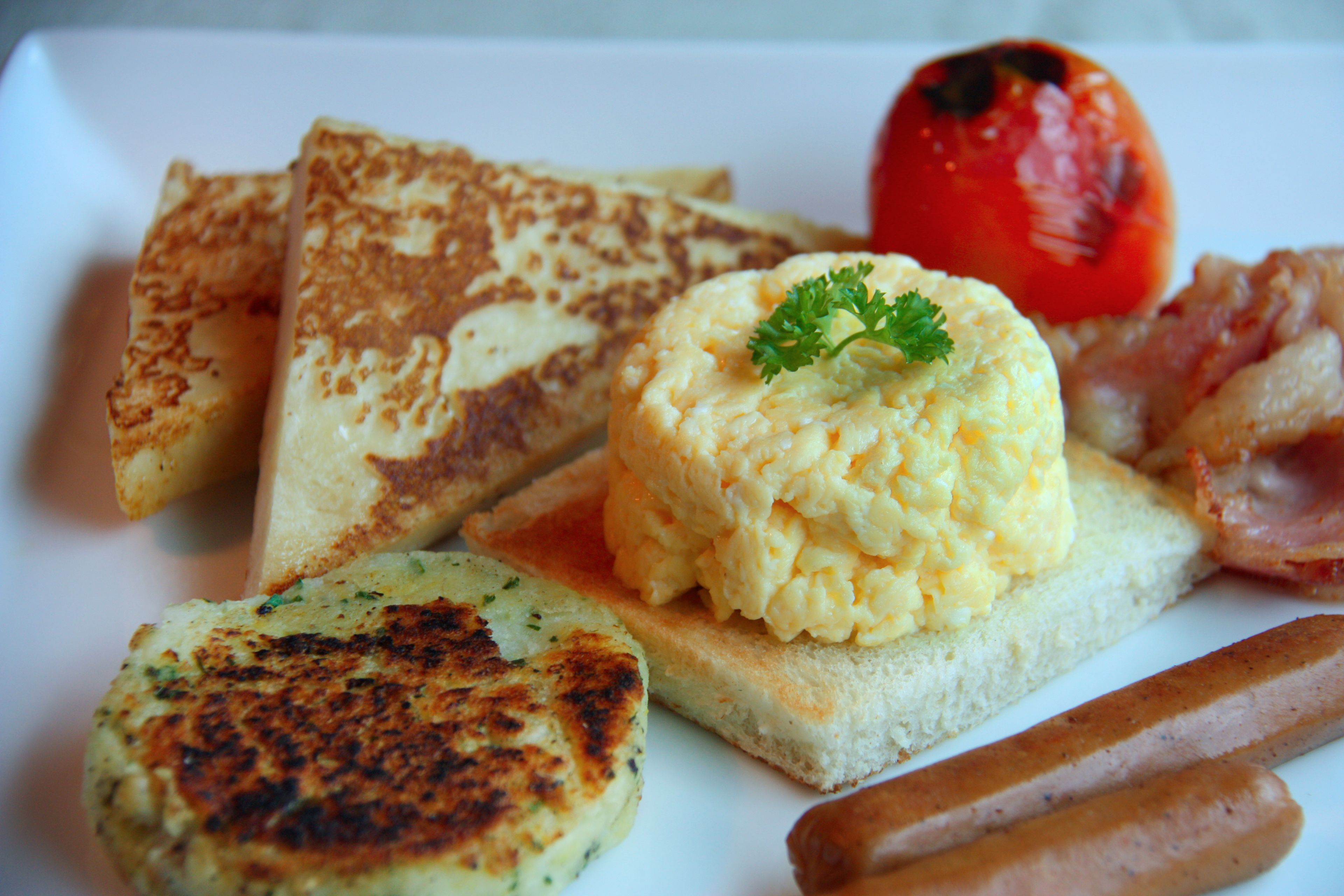 A breakfast plate with toast, scrambled eggs, bacon, a tomato, and hash browns.