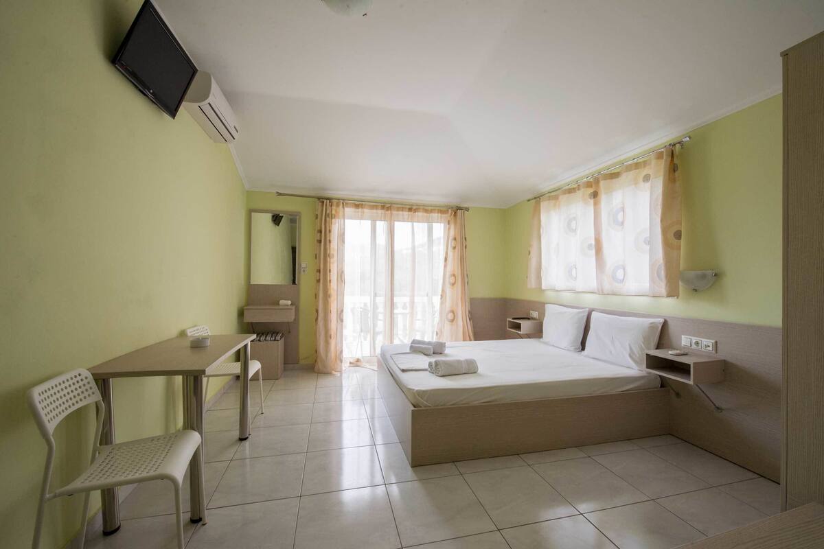 Ein Hotelzimmer mit Bett, Schreibtisch, Stuhl, Fernseher und einem Vorhangfenster.