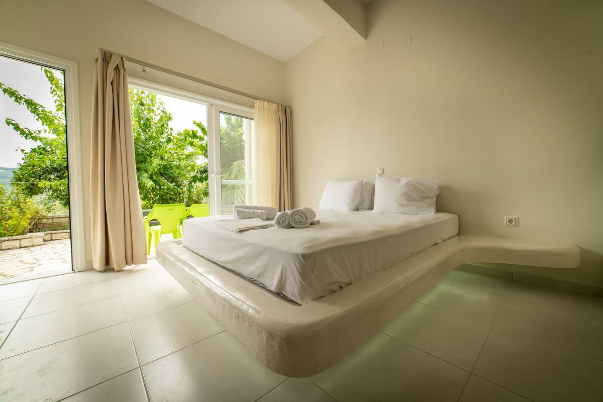 Ein Schlafzimmer mit einem großen Bett, einer eingebauten Sitzbank und Blick auf Grün.