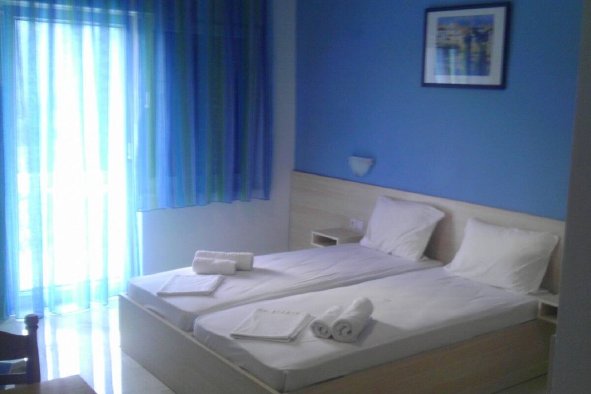 Ein Hotelzimmer mit zwei Betten, einem Nachttisch, einer Lampe und einem Fenster mit blauen Vorhängen.
