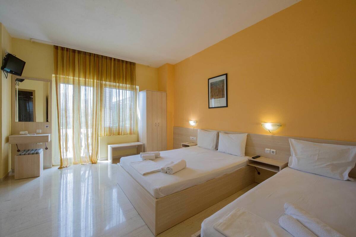 Ein Hotelzimmer mit einem großen Bett, einem Nachttisch, einem Kleiderschrank und einem an der Wand befestigten Fernseher.