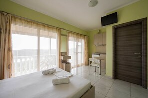 A hotel room with a bed, a desk, a chair, a TV, and a door.