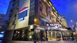 Un hotel moderno con un letrero llamativo que dice "Terminal Hotel". Cuenta con fachada de vidrio, área de estar al aire libre y una entrada bien iluminada.