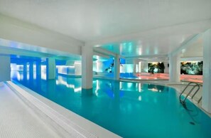 Una piscina interior con agua cristalina, rodeada de paredes y columnas blancas, y vista al cielo nocturno.