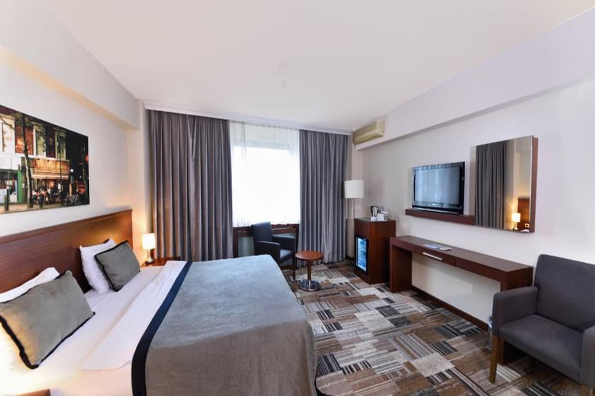 A hotel room with a large bed, a desk, a TV, and a sofa.