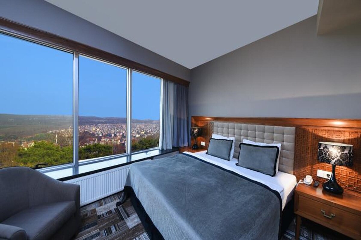 Una habitación de hotel moderna con una cama grande, vistas a la ciudad y una zona de descanso acogedora.