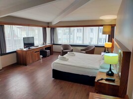 Habitación de hotel con cama, escritorio, televisión, sillas y lámpara.