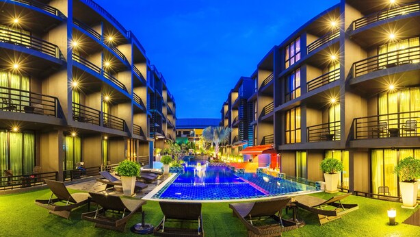 Une cour d’hôtel avec une piscine, des chaises longues et des plantes en pot.