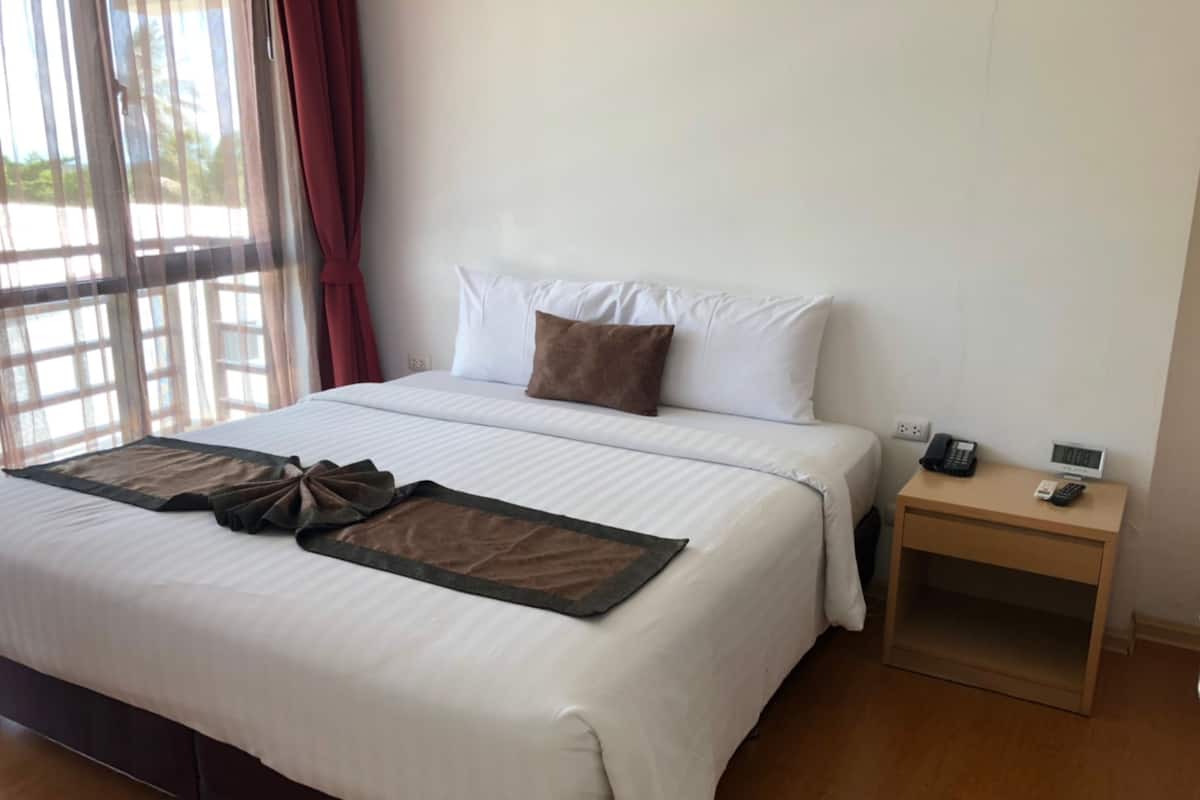 A hotel room with a large bed, a bedside table with a phone and a digital device, and a window with curtains.