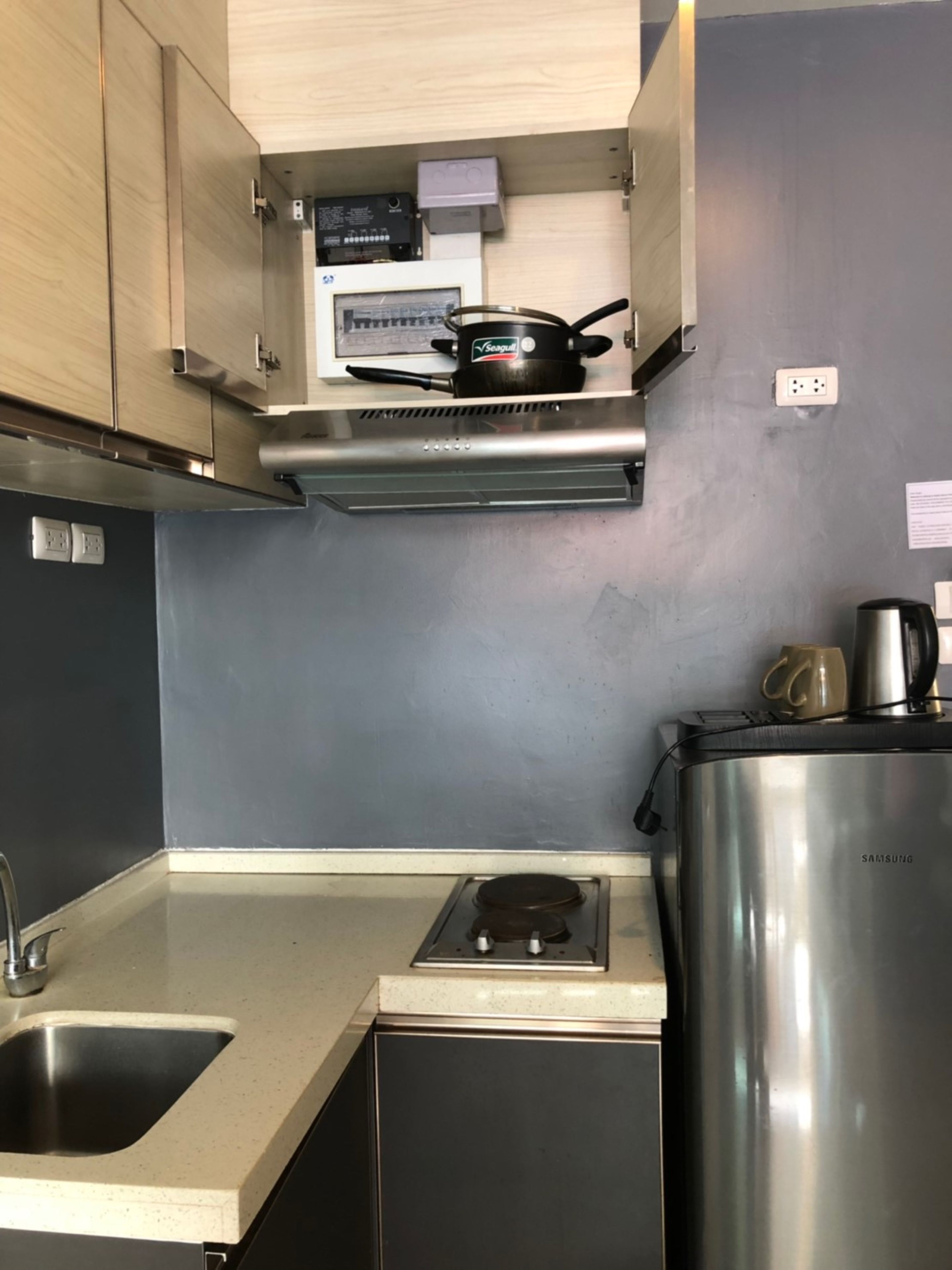 A compact kitchen with a stainless steel range hood, a built-in oven, a sink, and a refrigerator.