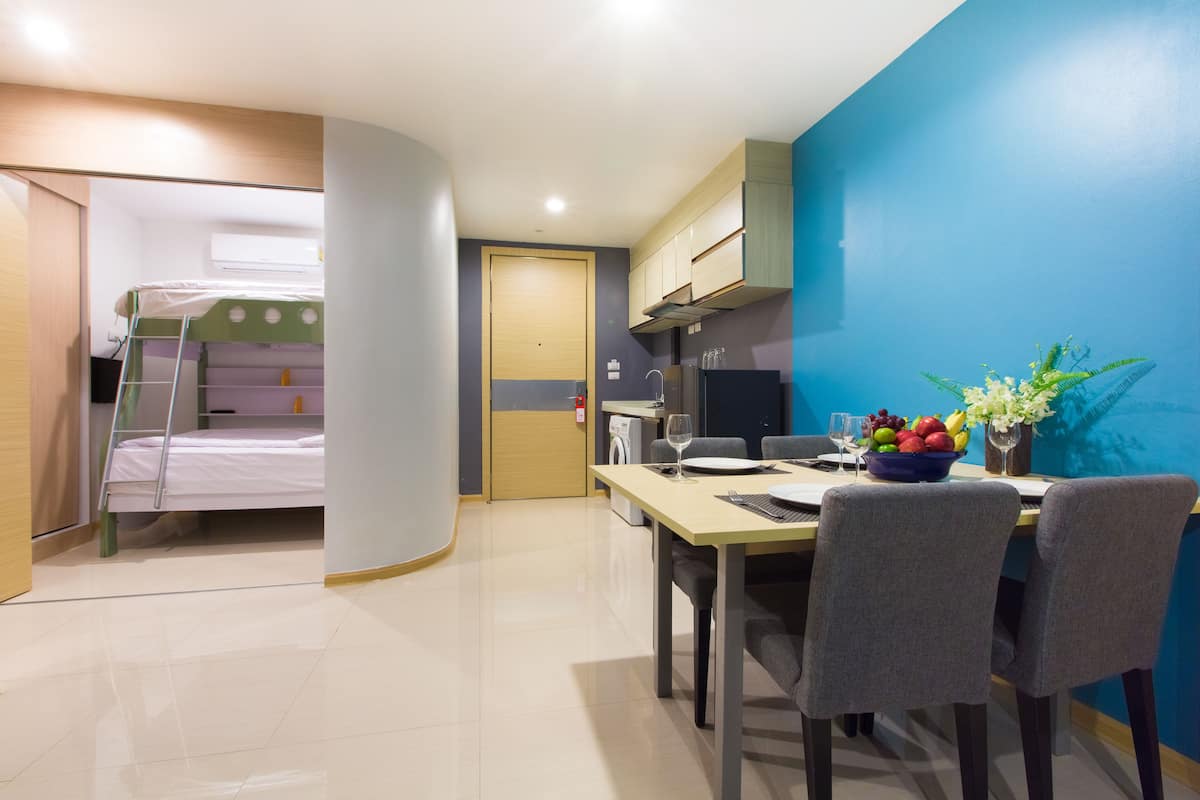A compact hotel room with a bunk bed, a dining area with a table and chairs, a small kitchen, and a blue accent wall.