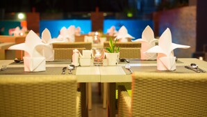 Un espace repas avec des tables dressées pour deux personnes, agrémentées de serviettes blanches, de couverts et d’une petite plante servant de décoration centrale.