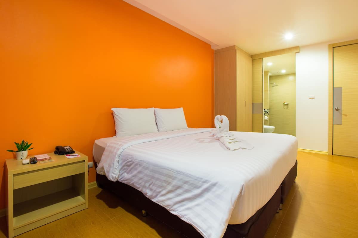 A hotel room with a bed, bedside table, and a small plant.