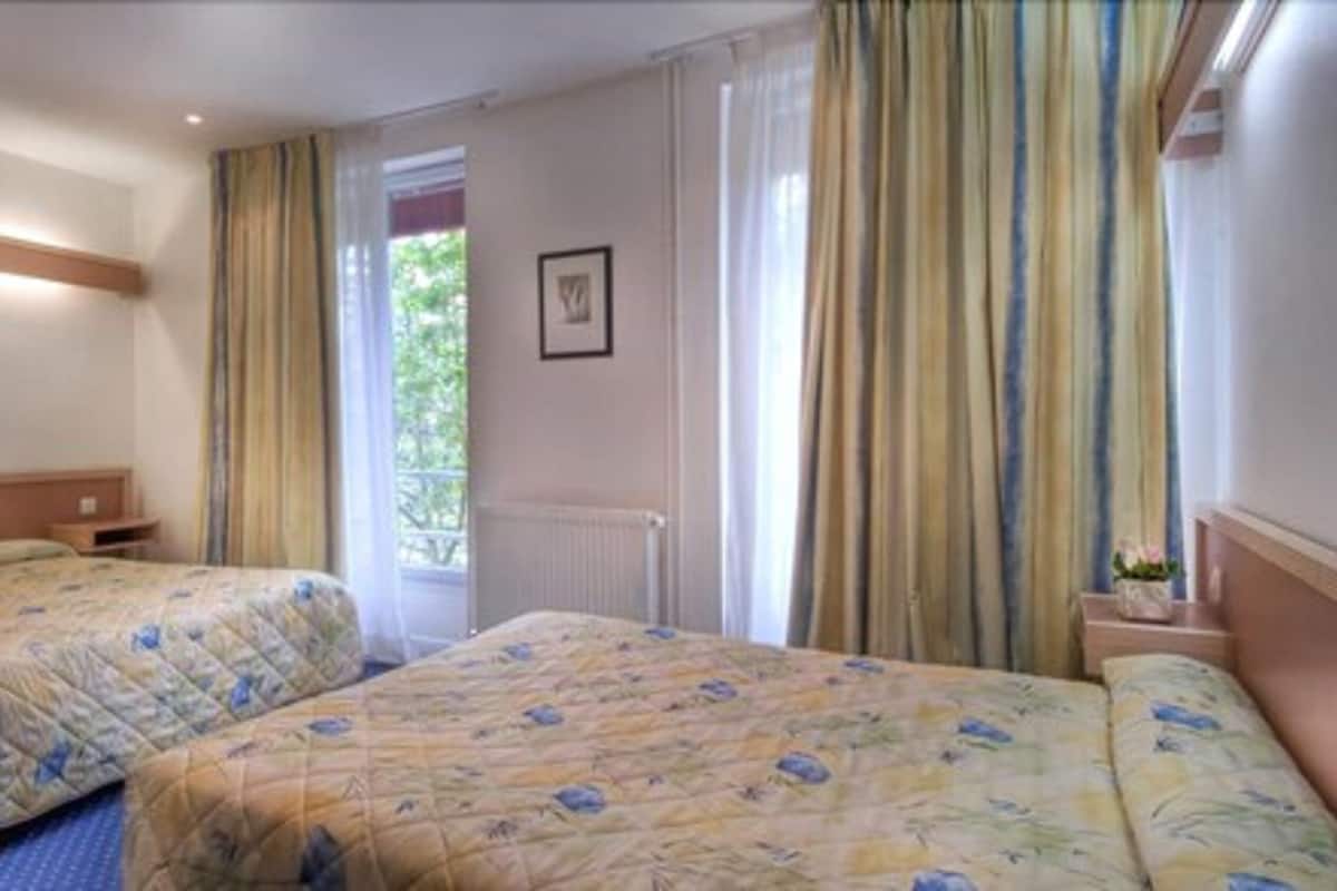 A hotel room with two beds, a window with curtains, a radiator, and a framed picture on the wall.