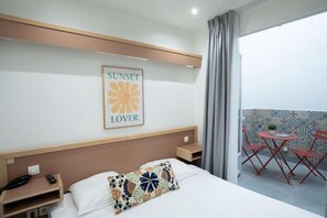 A hotel room with a bed, a nightstand, a phone, a framed picture on the wall, and a balcony with a table and chairs. - Hotel Edgar Quinet (Paris)