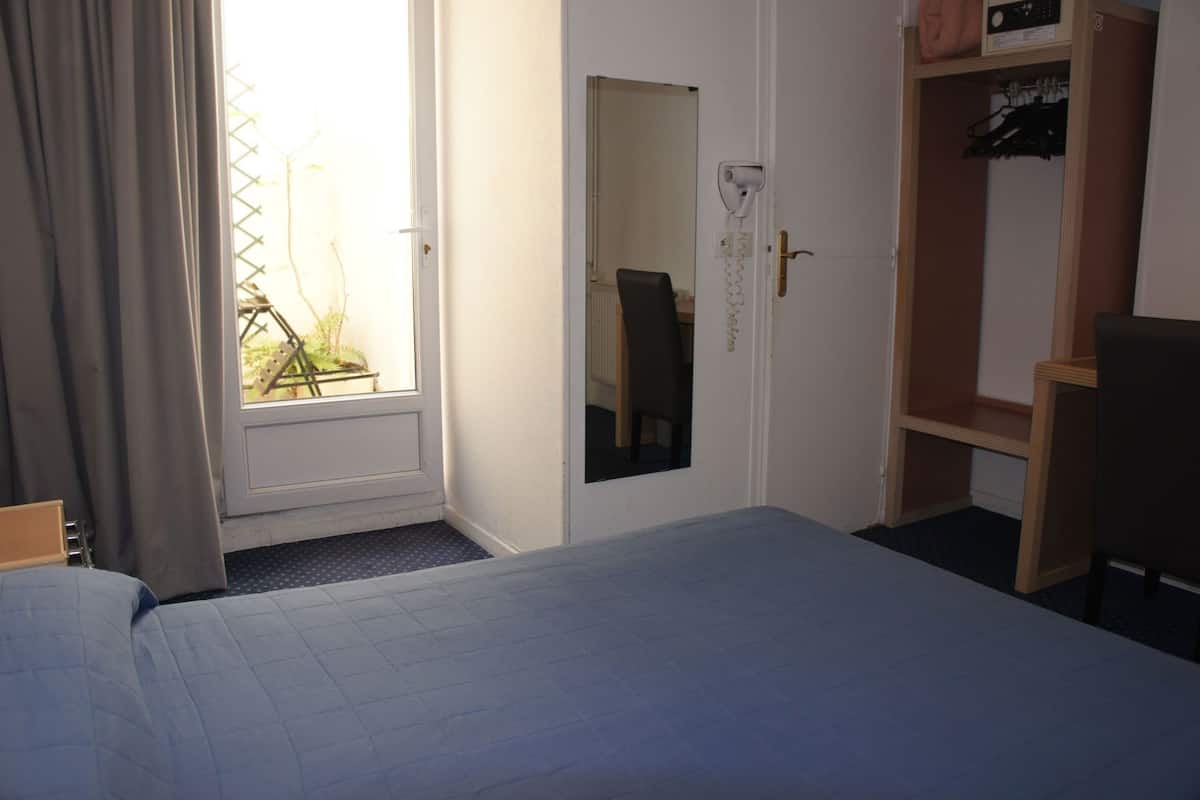 A hotel room with a bed, a desk, a chair, a wardrobe, and a window with curtains.