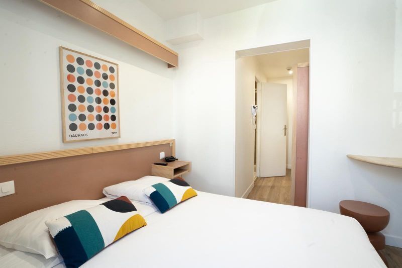 Habitación de hotel con cama, mesita de noche, una obra de arte enmarcada en la pared y una puerta que da a otra habitación.