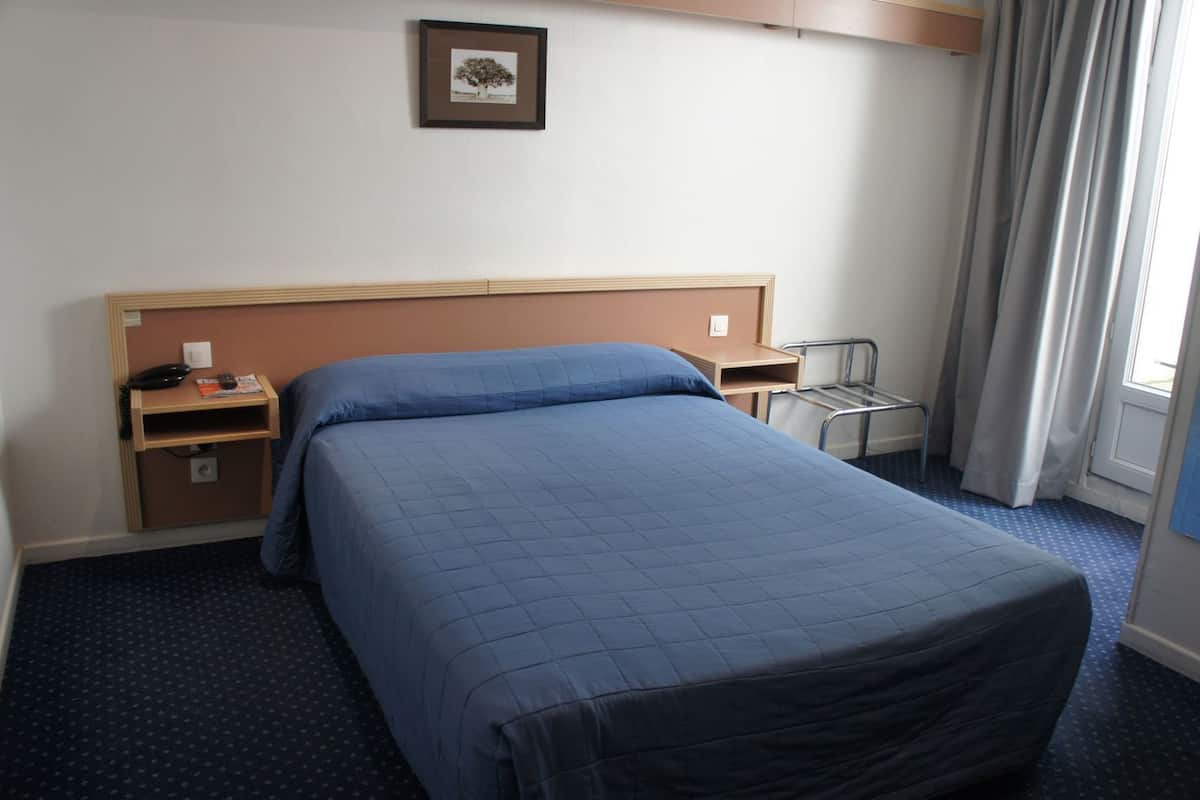 A hotel room with a bed, a desk, a chair, a telephone, and a picture on the wall.